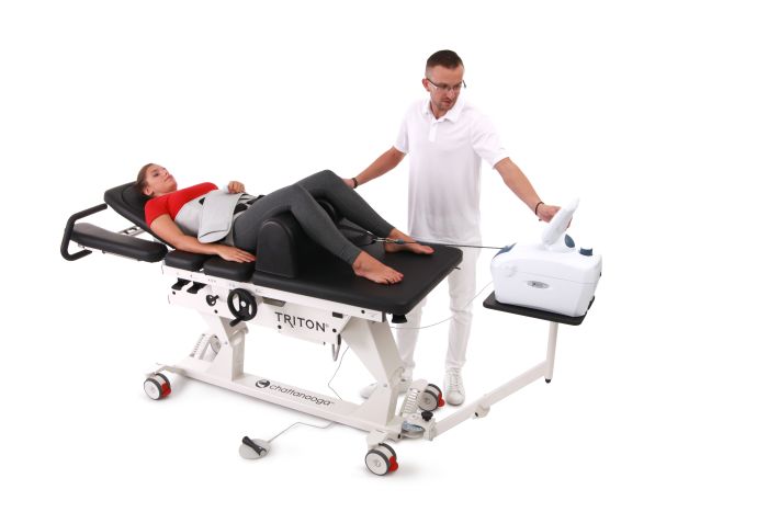 A woman lies on a therapy table with a belt on her waist while a technician operates a connected medical device.