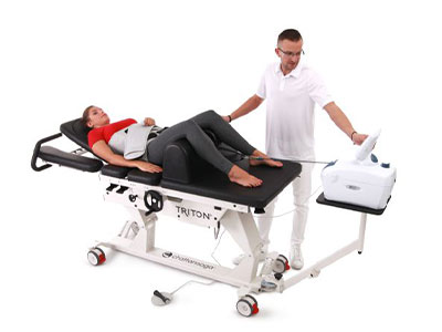 A woman lies on a Triton therapy table while a clinician operates a connected medical device.