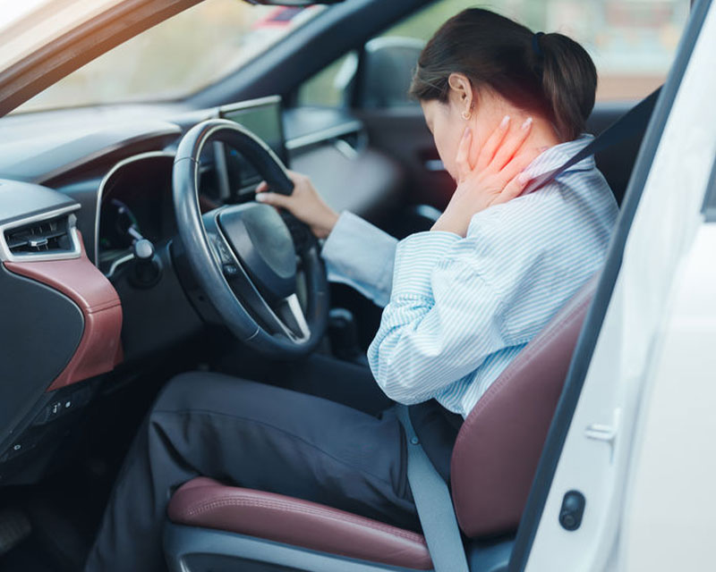 Woman sitting in a car holding her neck, appearing to be in pain or discomfort.